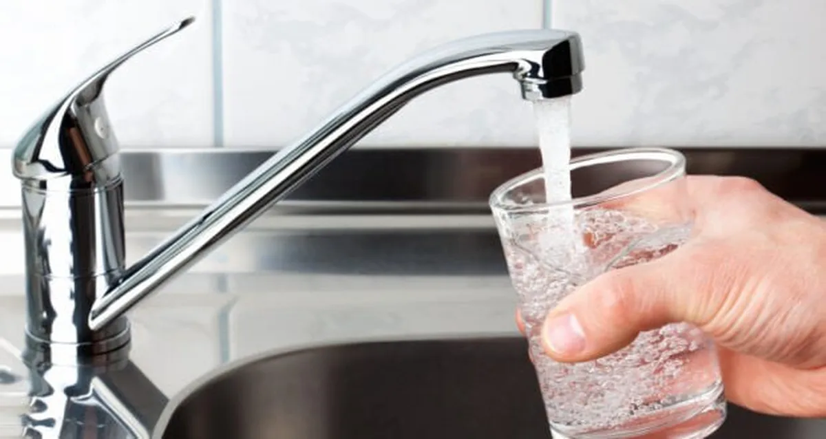 Рука наливає воду з крана в склянку
