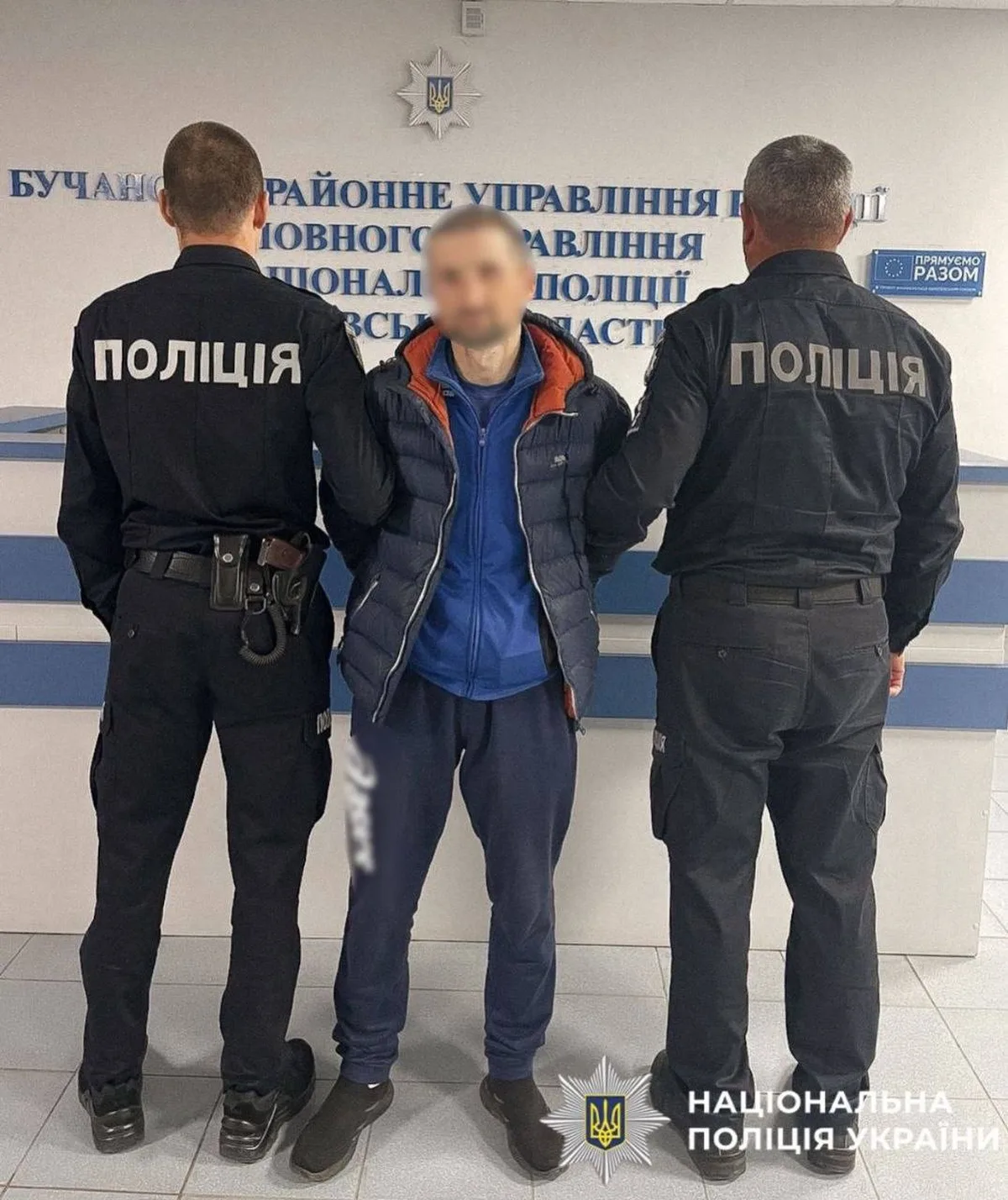 Чоловік у синій куртці між двома поліцейськими в офісі