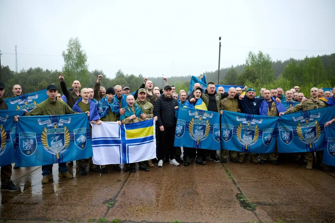 Група людей з синіми прапорами та символікою на грунтовій дорозі