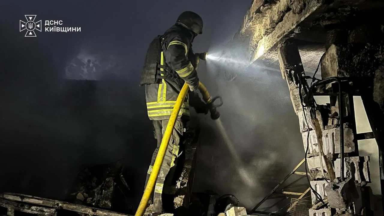 Рятувальник гасить пожежу в пошкодженій будівлі вночі