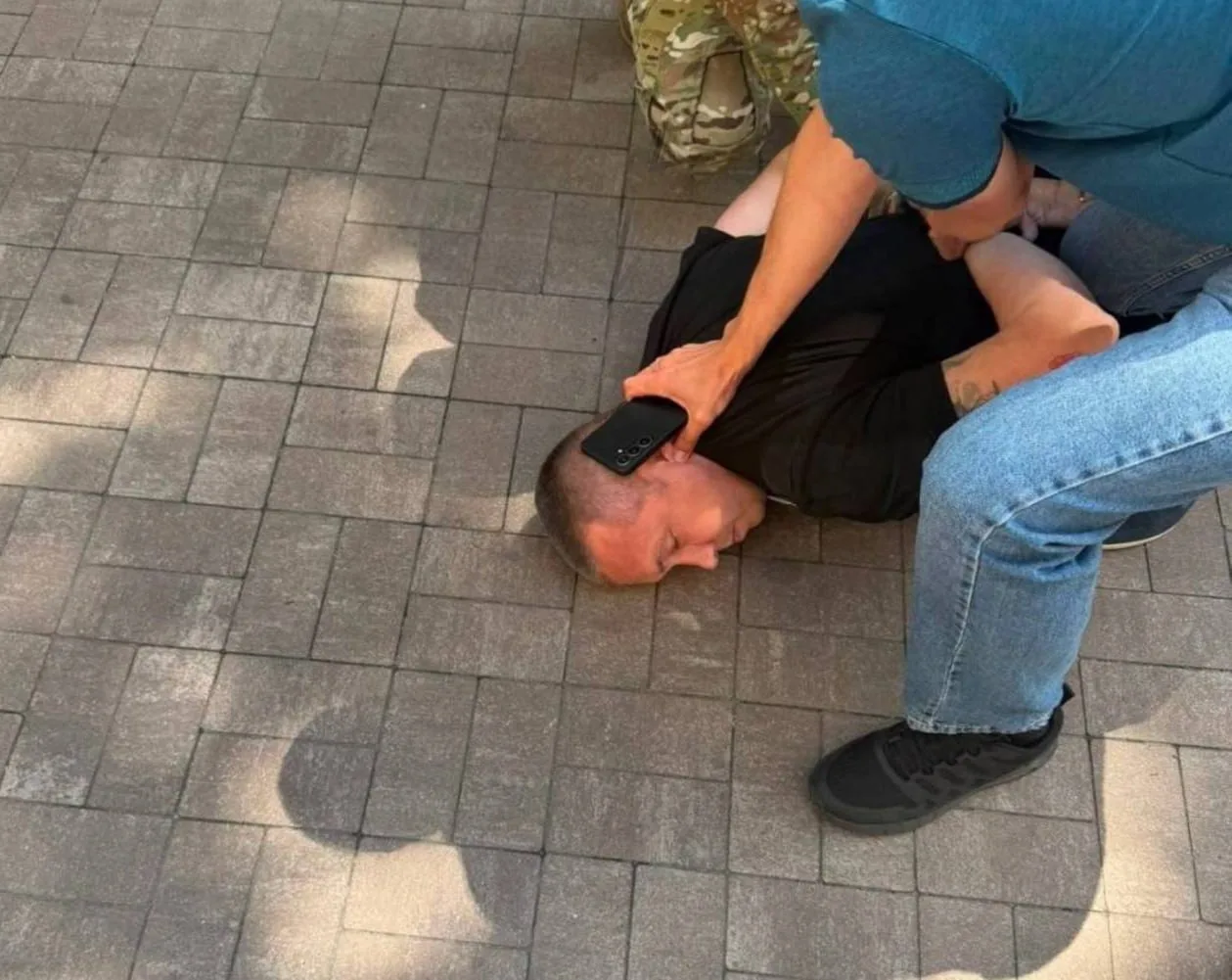 Людина в чорній футболці сидить на плитці з телефоном