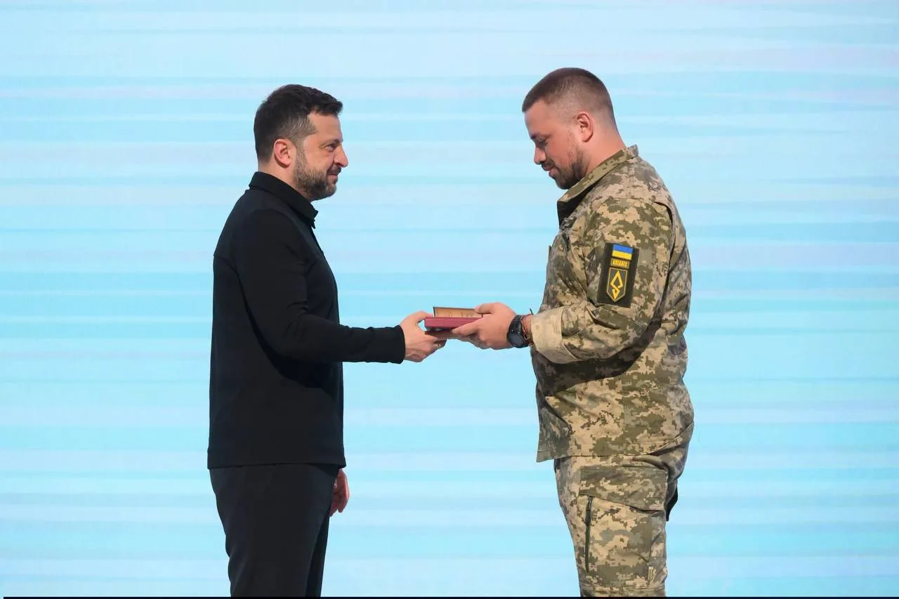 Чоловік у чорному піджаку вручає нагороду військовому