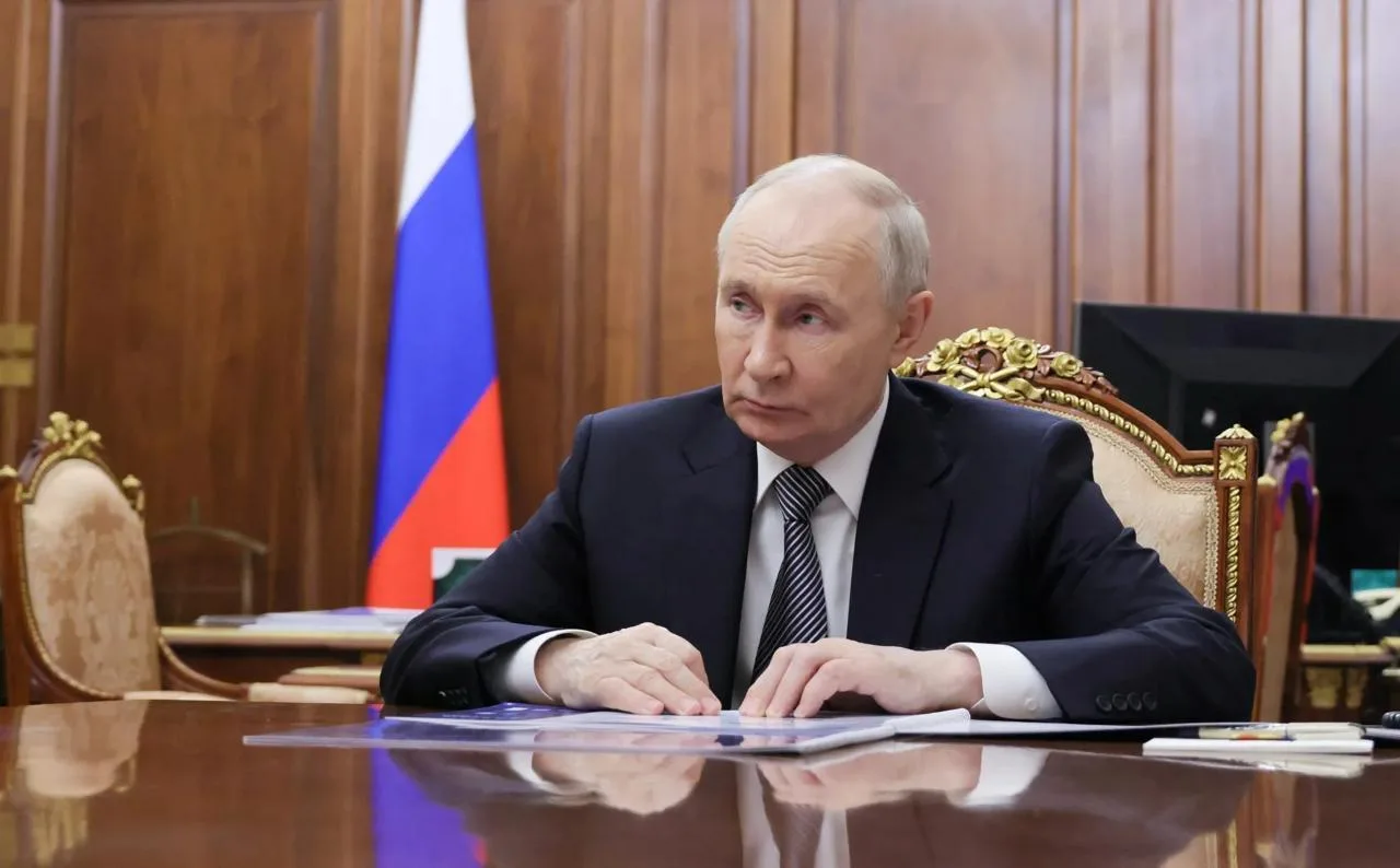 Чоловік у темному костюмі за столом з прапором Росії