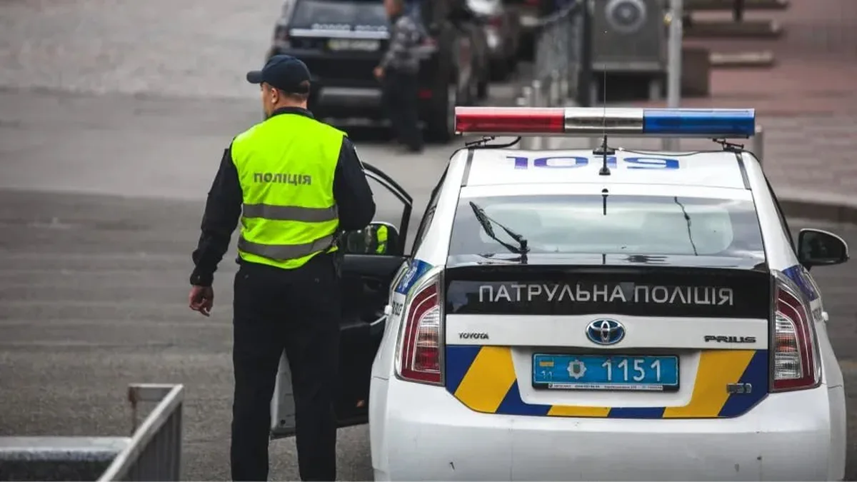 Поліцейський у жовтому жилеті біля патрульного автомобіля