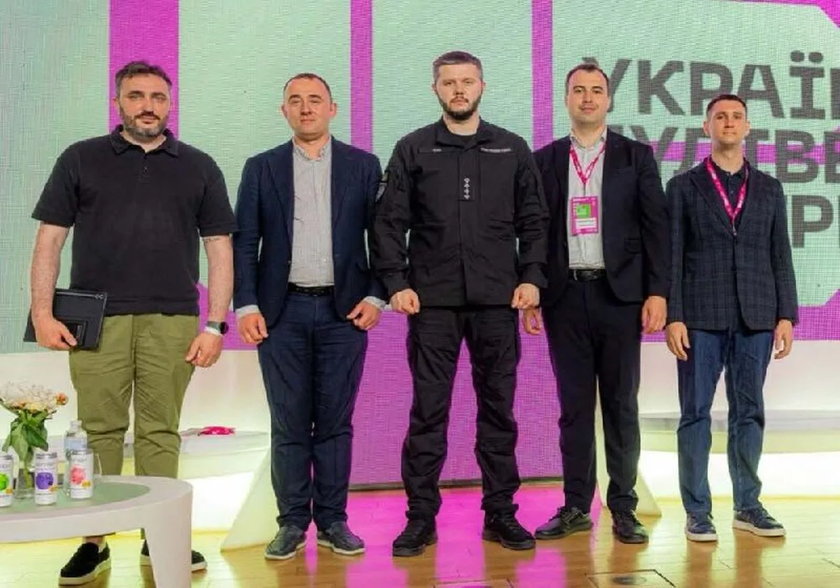 П'ять чоловіків стоять на сцені на фоні рожевого екрана