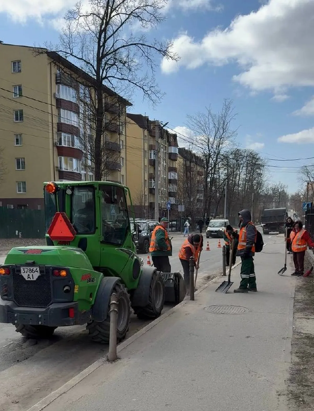 Робітники в помаранчевих жилетах біля зеленого трактора