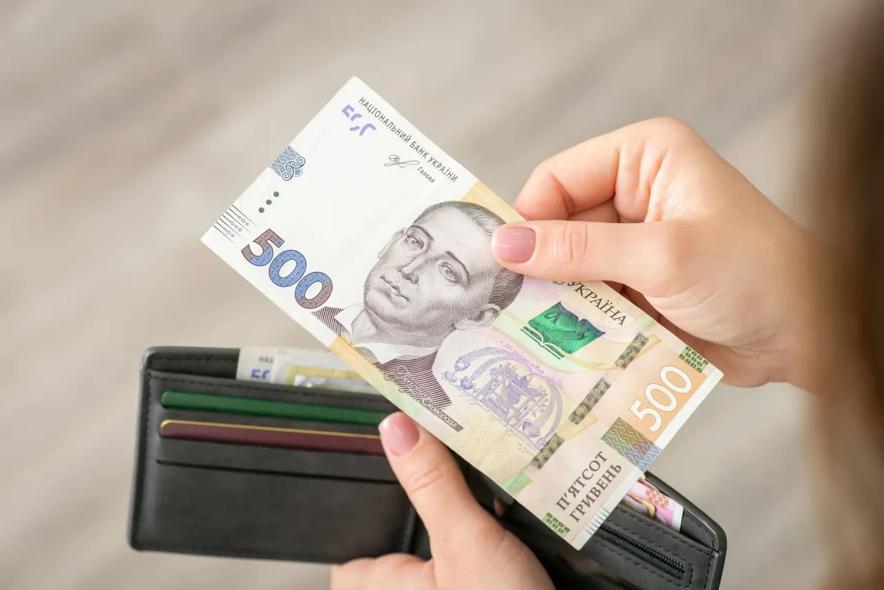 Рука дістає гривні з чорного гаманця