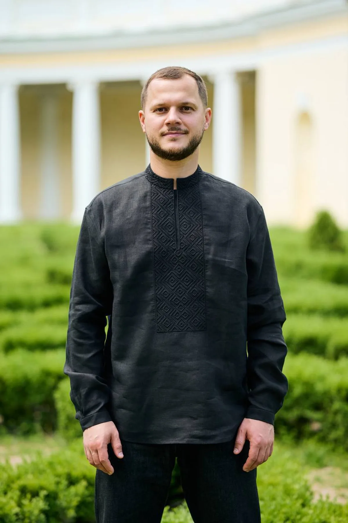 Чоловік у чорній вишиванці на фоні будівлі