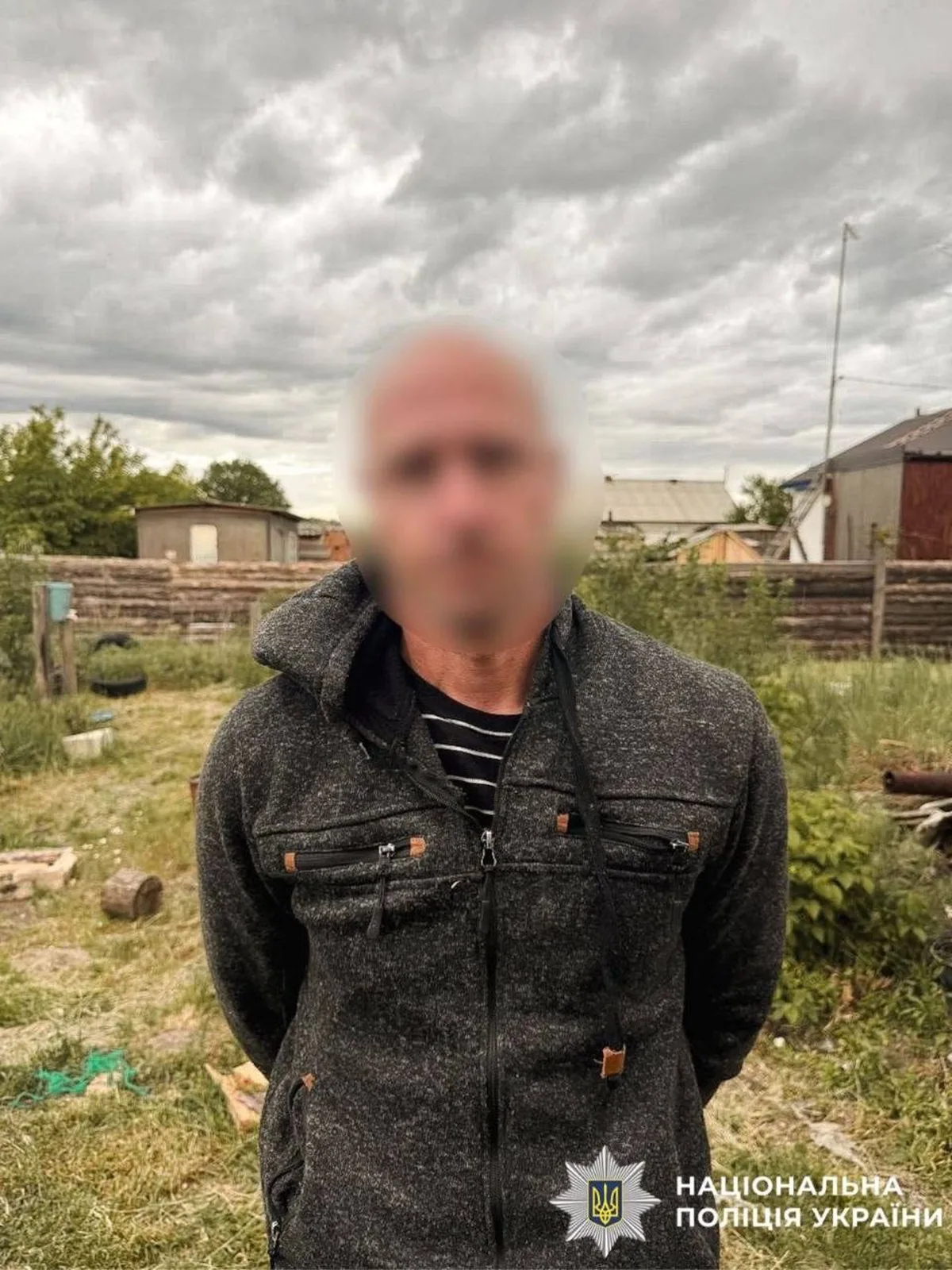 Чоловік у сірій куртці на фоні приватних будинків