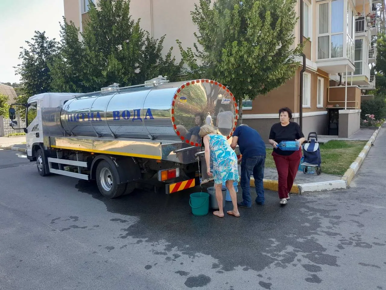 Автоцистерна з питною водою біля будинку, люди набирають воду в контейнери