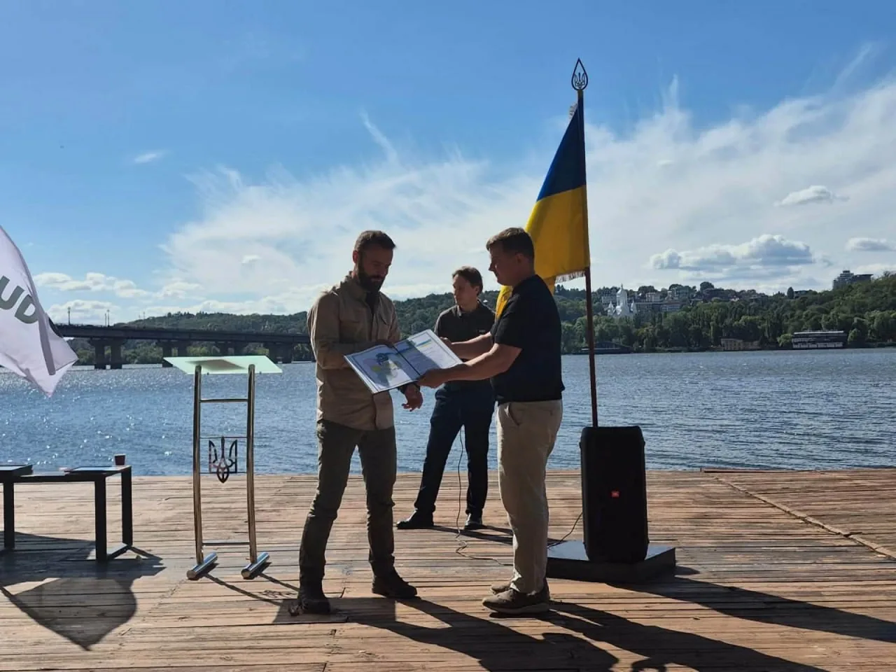 Троє людей на причалі біля українського прапора розглядають документ