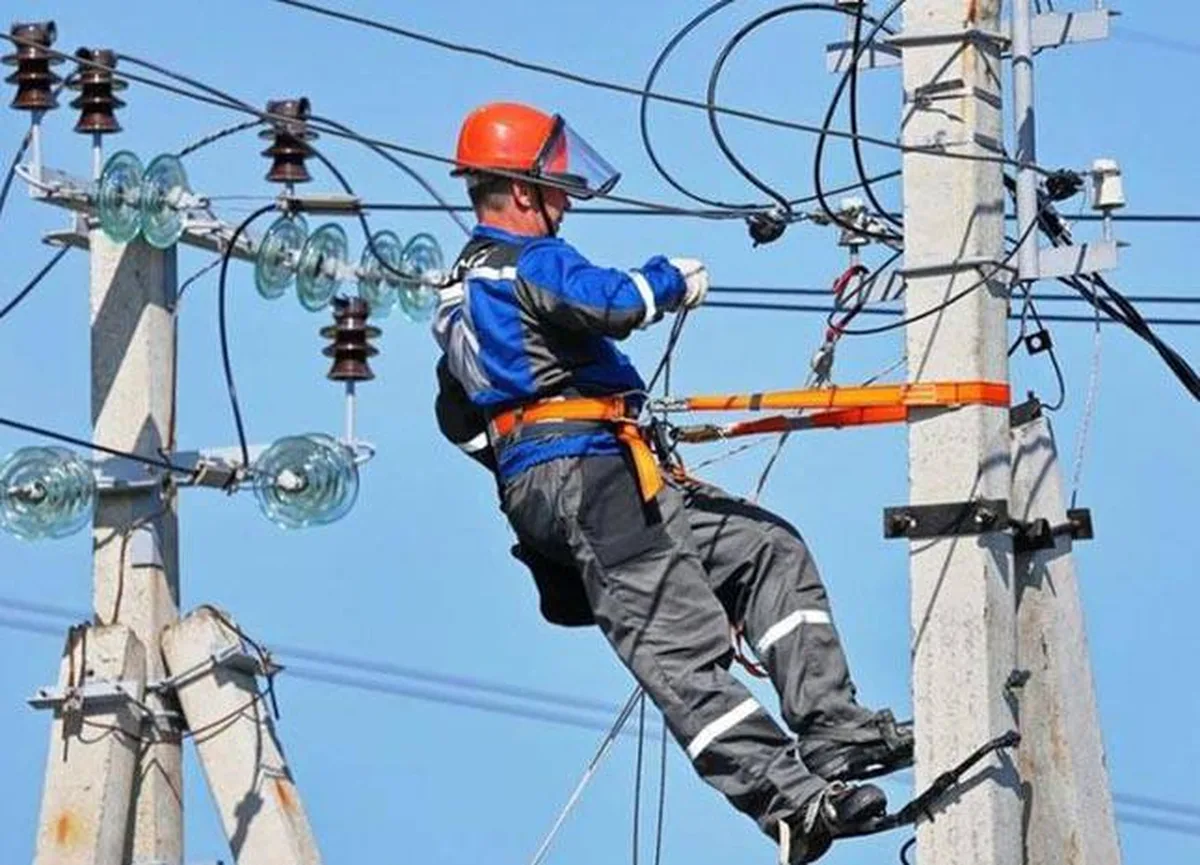 Електромонтер у захисному спорядженні на електроопорі