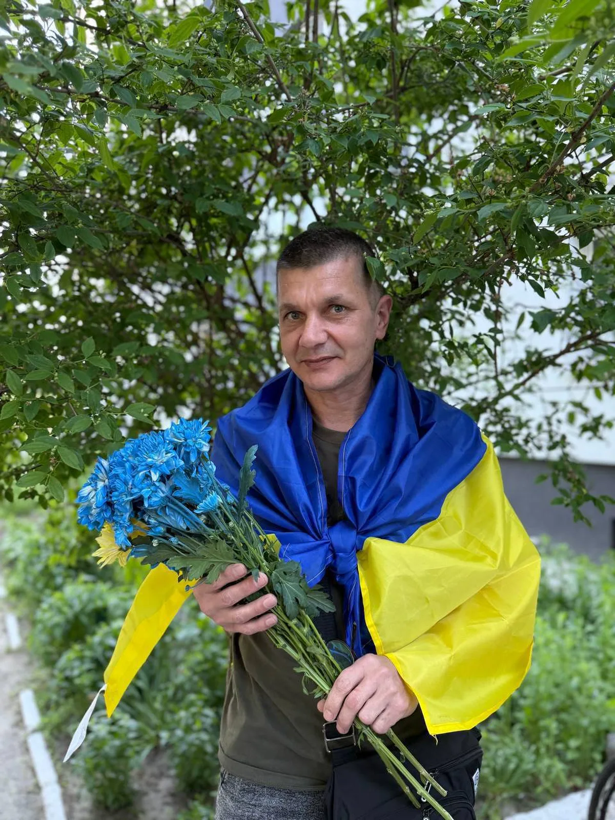 Чоловік з букетом синіх квітів у жовто-синьому одязі