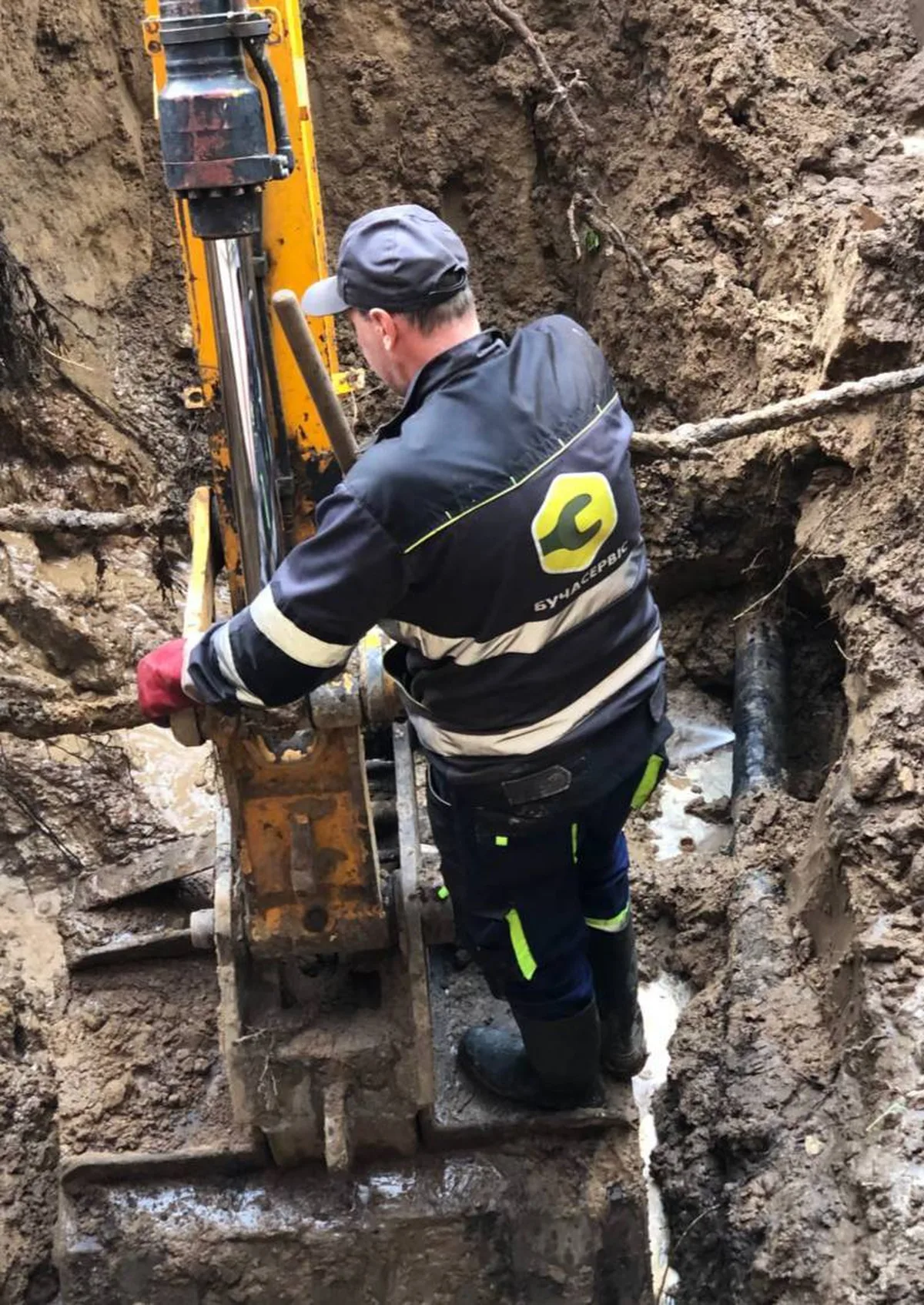 Робітник з інструментом в траншеї біля пошкодженого водопровідного трубопроводу