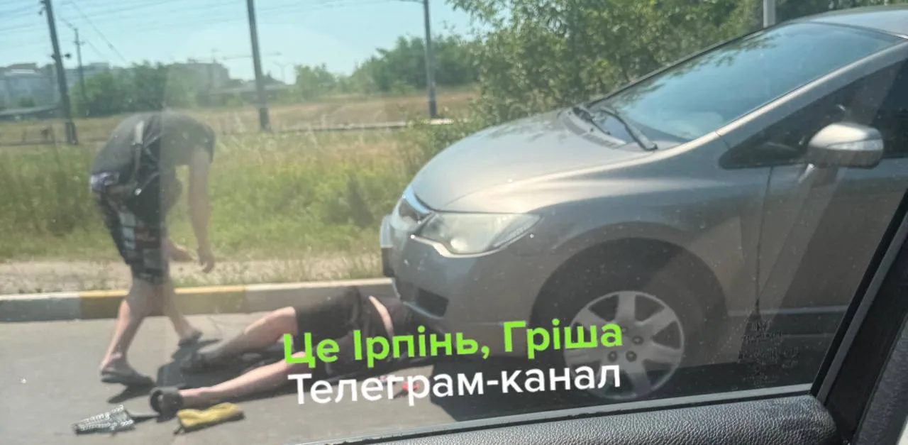 Людина біля пошкодженого автомобіля на дорозі з вибоїною