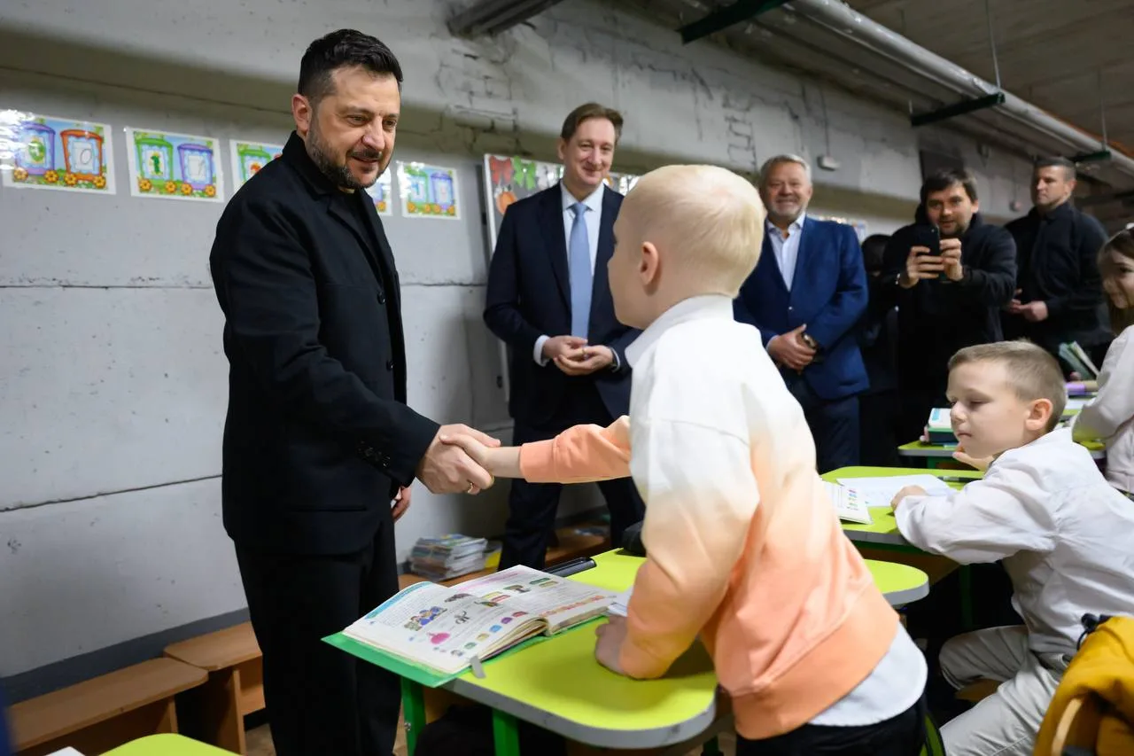 Чоловік у чорному костюмі пожимає руку дитині в класі