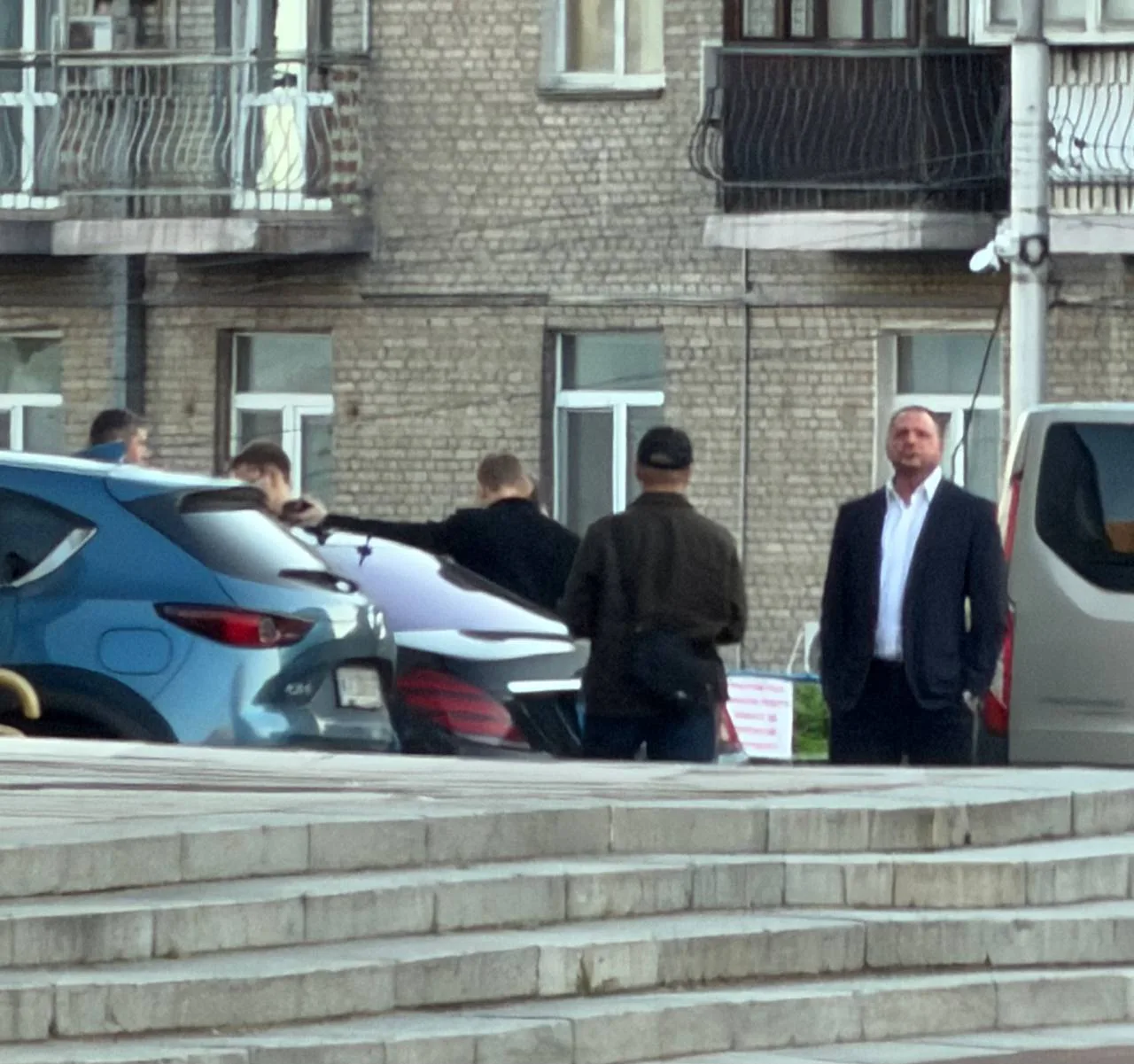 Люди біля припаркованих автомобілів перед будівлею
