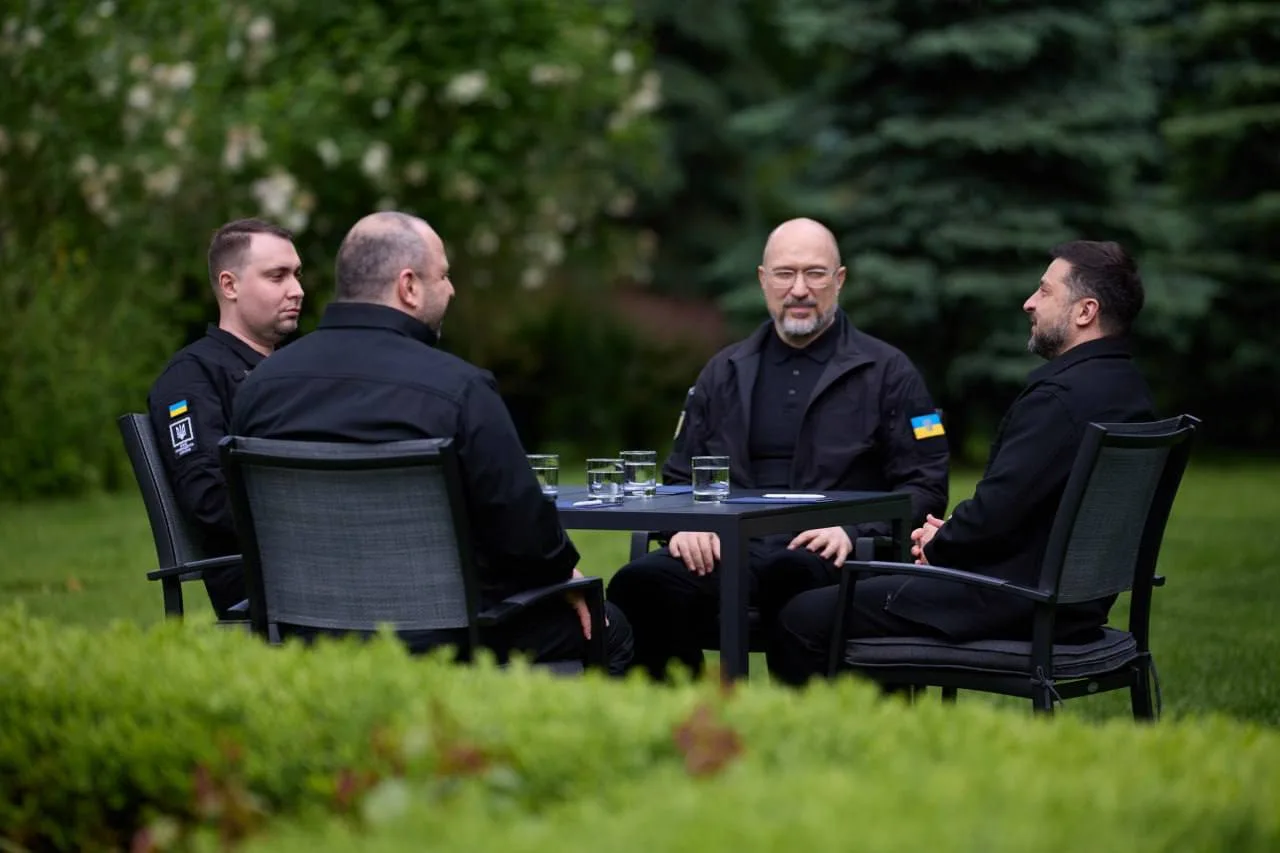 Чотири чоловіки в чорному сидять на стільцях у парку