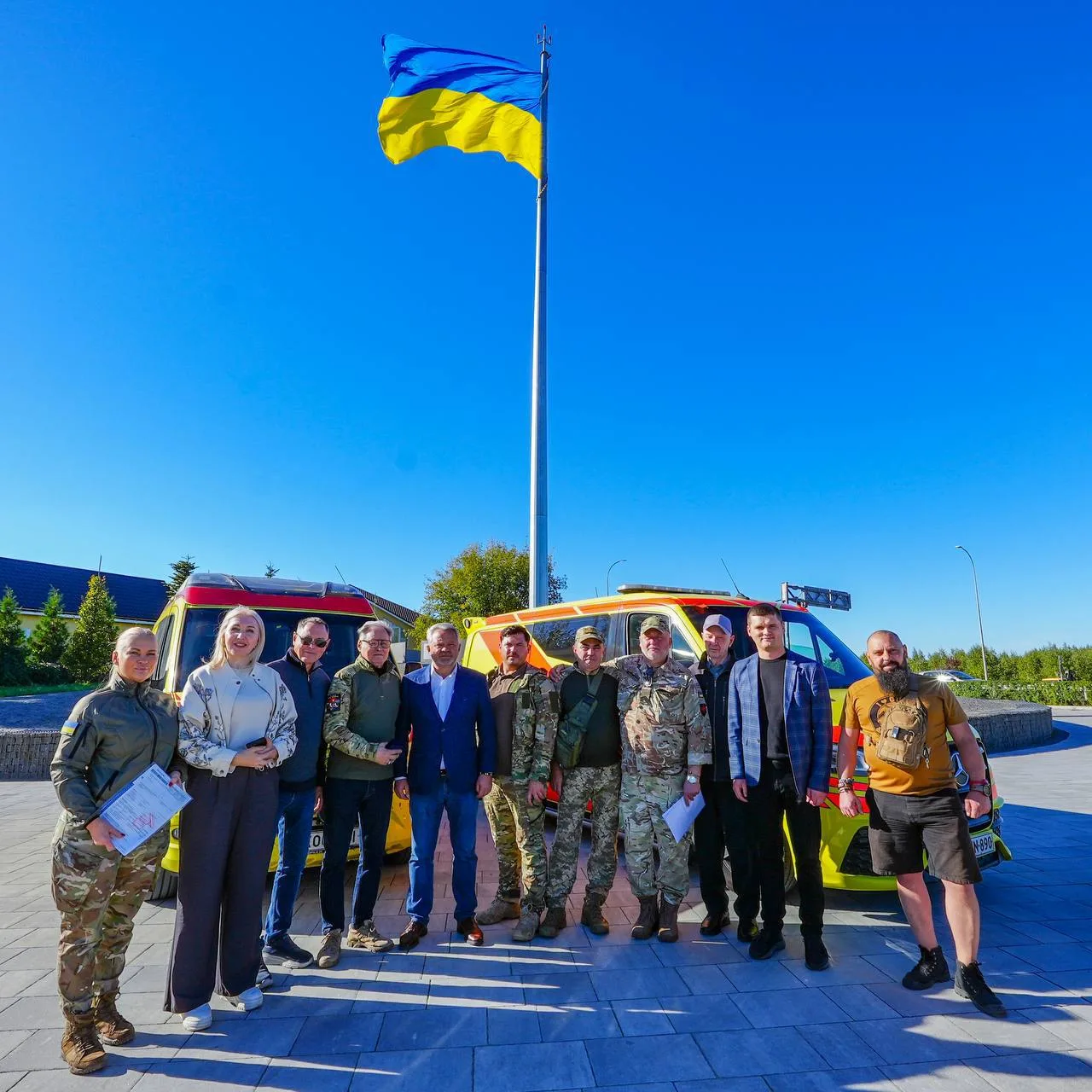 Група людей стоїть біля машин швидкої допомоги під українським прапором