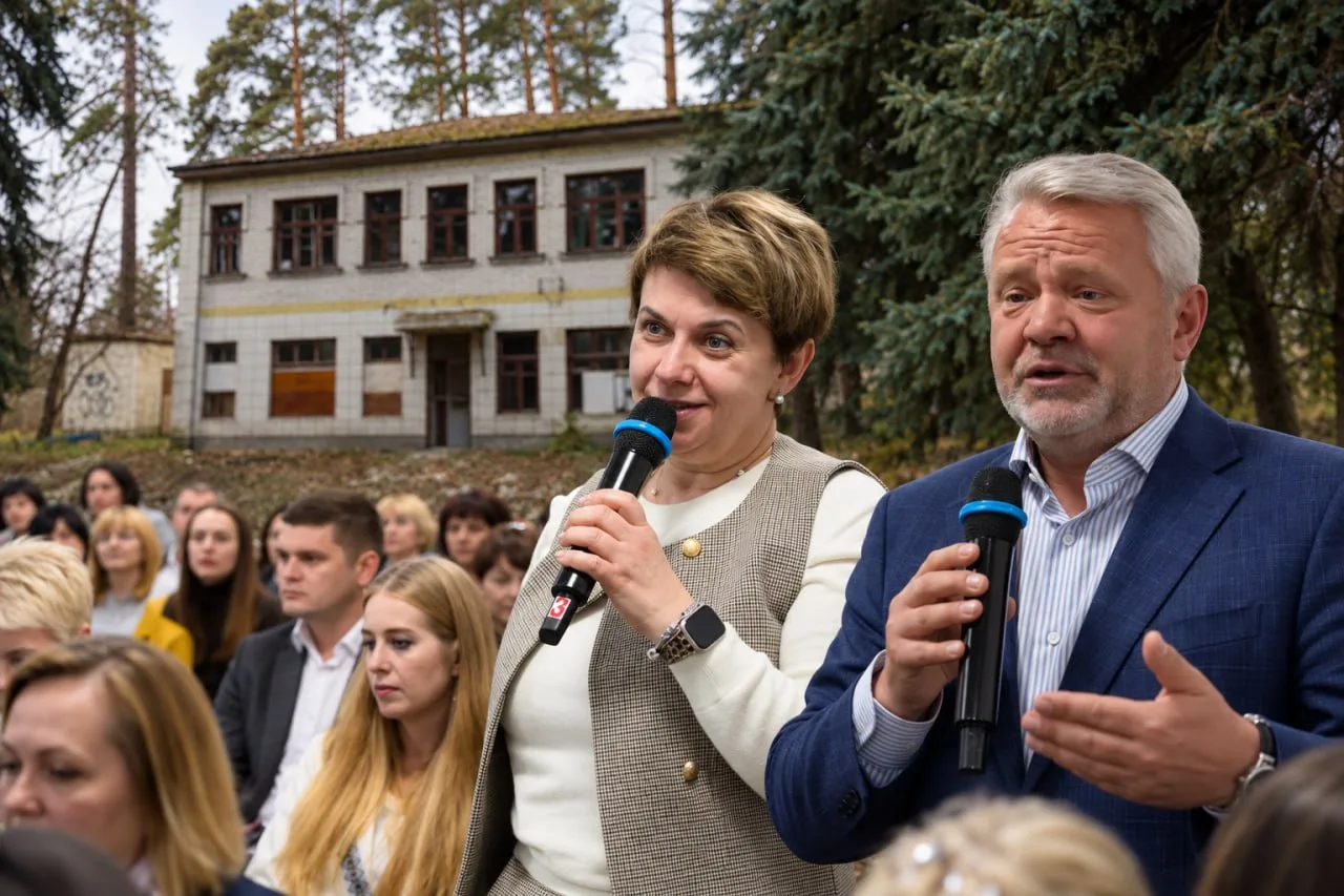 Двоє чоловіків зі мікрофонами виступають перед натовпом людей біля старої будівлі