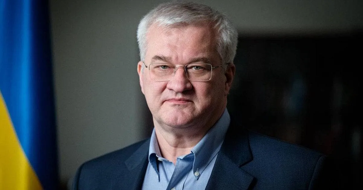 Чоловік середнього віку в темному піджаку біля прапора України