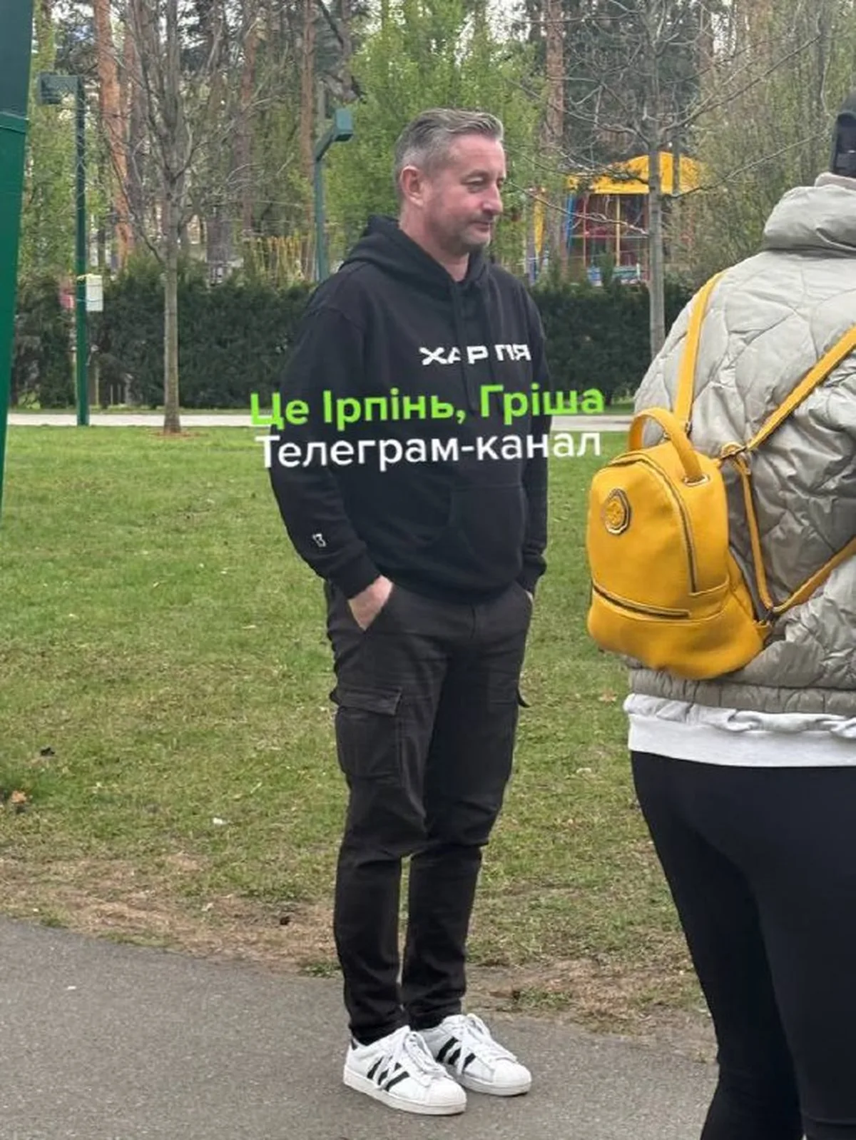 Чоловік у чорній худі розмовляє з людиною в парку