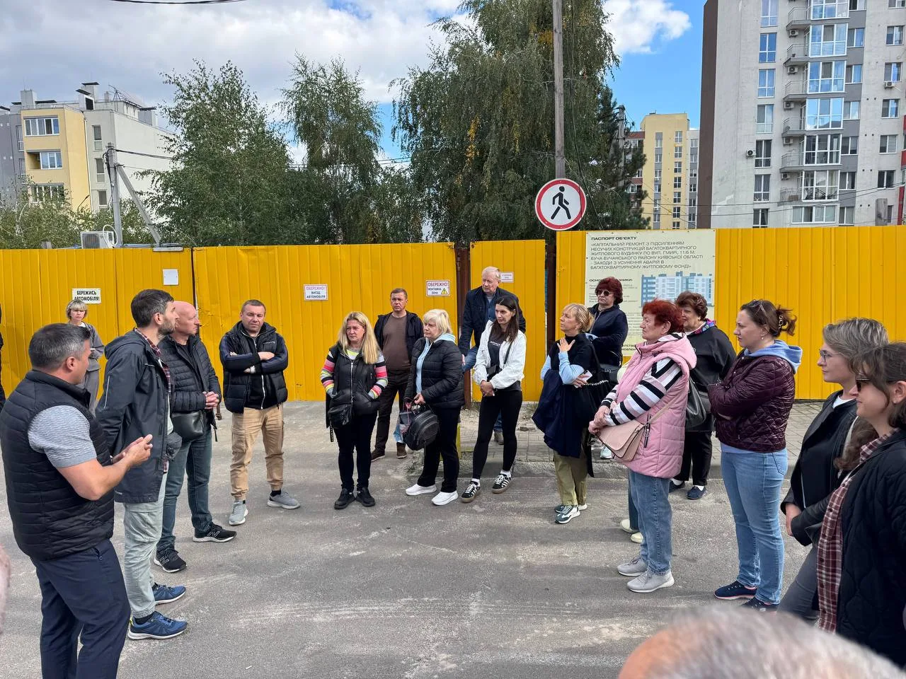 Група людей стоїть біля жовтого паркану на будмайданчику