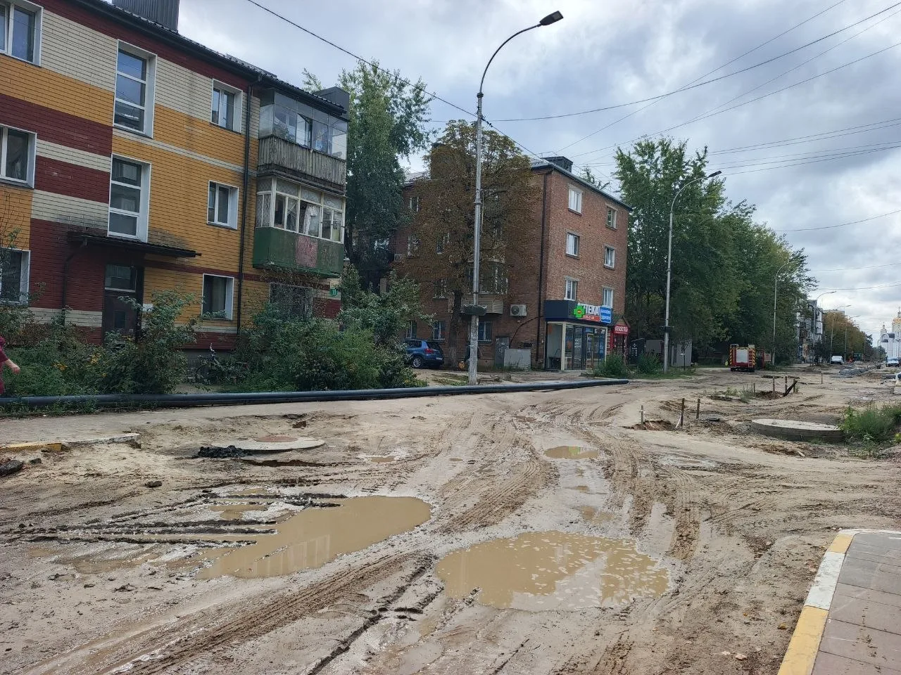 Розкопана вулиця з грунтом і калюжами води біля житлових будинків