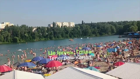 Пляж з багатьма людьми та парасольками біля річки