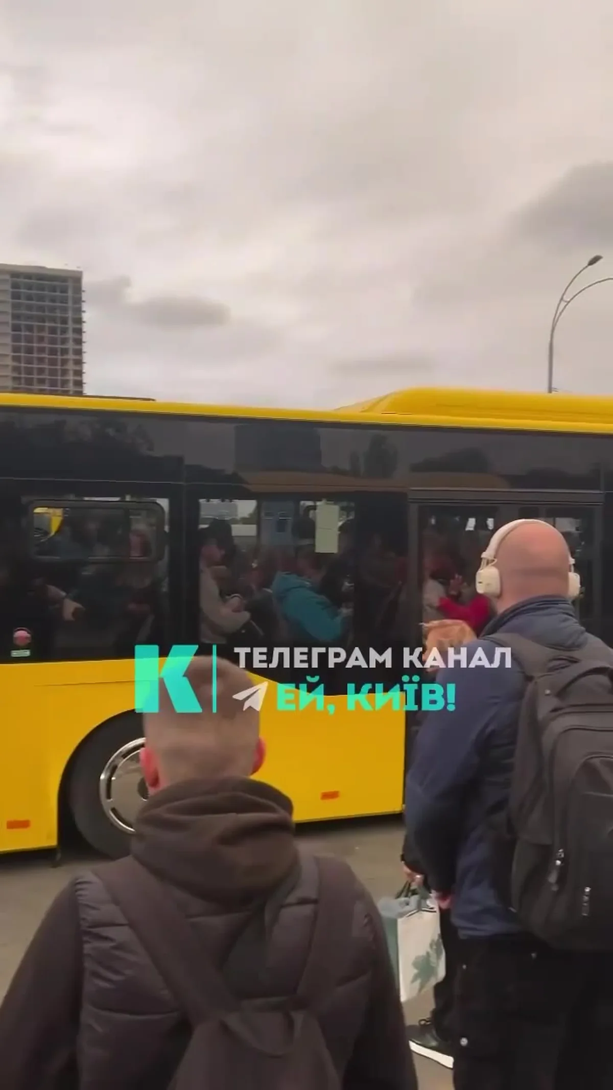 Люди чекають біля жовтого автобуса на зупинці