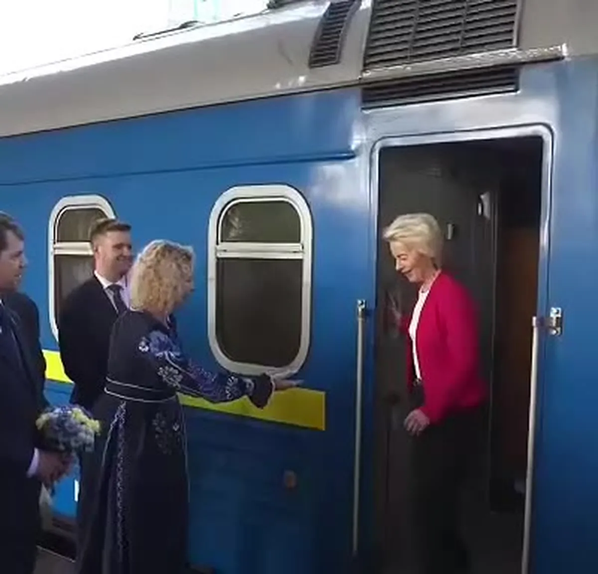 Люди біля входу до поїзда, жінка в червоному піджаку
