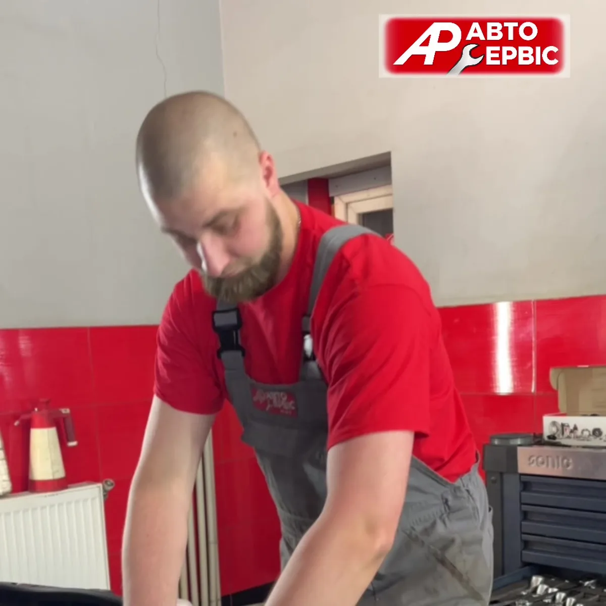 Механік в червоній робочій формі в автосервісі