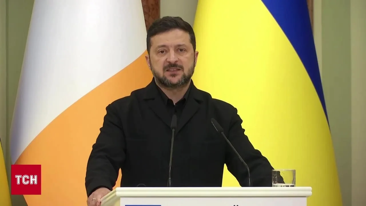 Чоловік у чорній сорочці біля мікрофона та прапорів