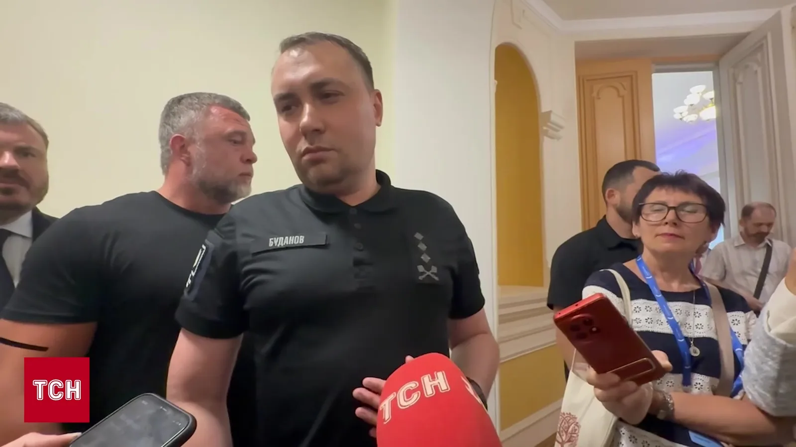 Чоловік у чорній футболці на прес-конференції з мікрофонами