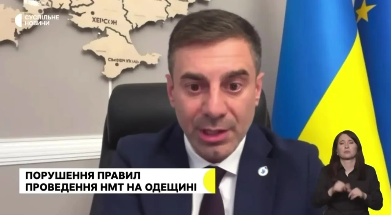 Чоловік у костюмі біля прапора України говорить в камеру
