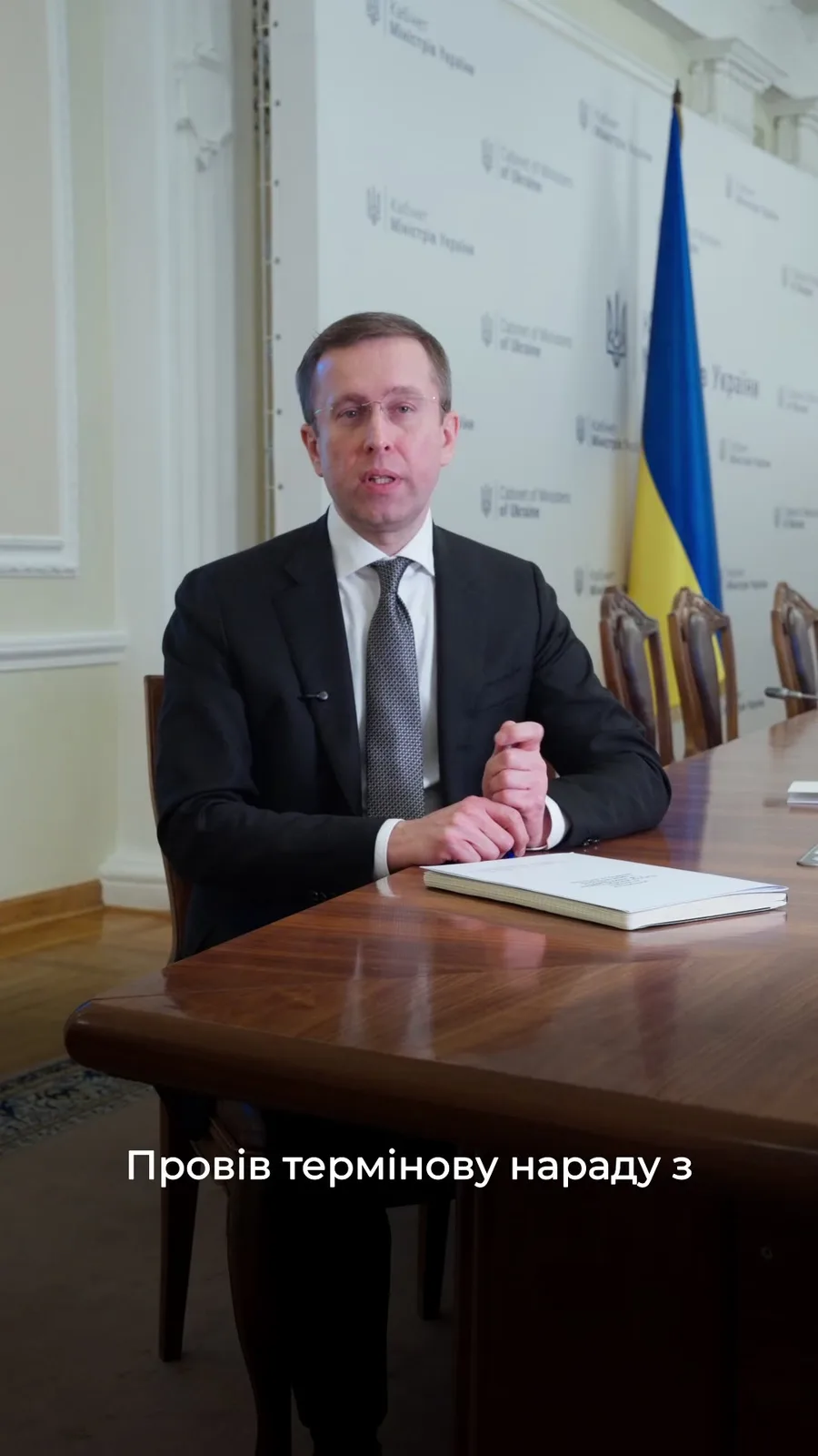 Чоловік у костюмі сидить за столом біля прапора України