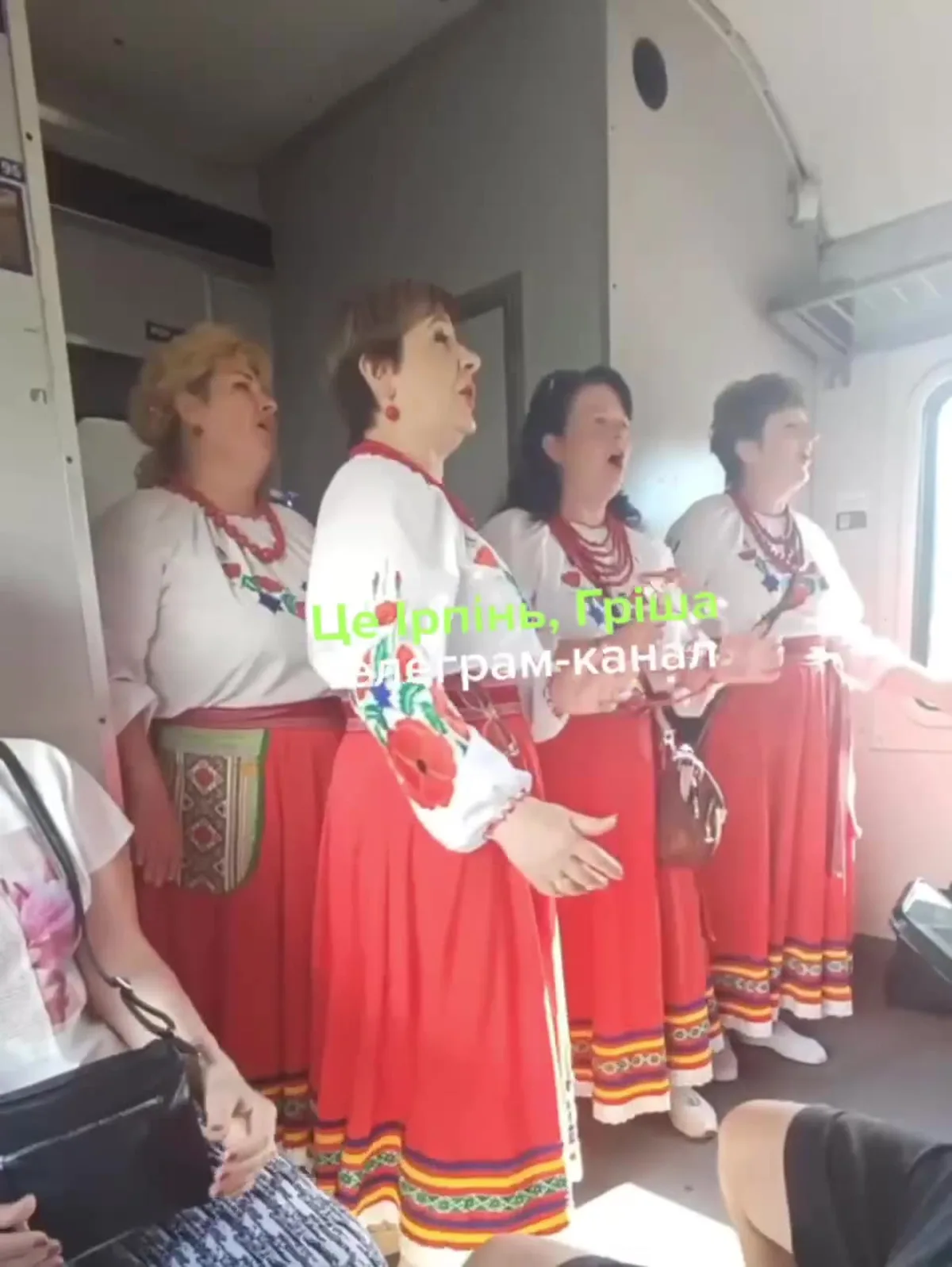 Чотири жінки в українських вишиванках і червоних спідницях співають у вагоні електрички