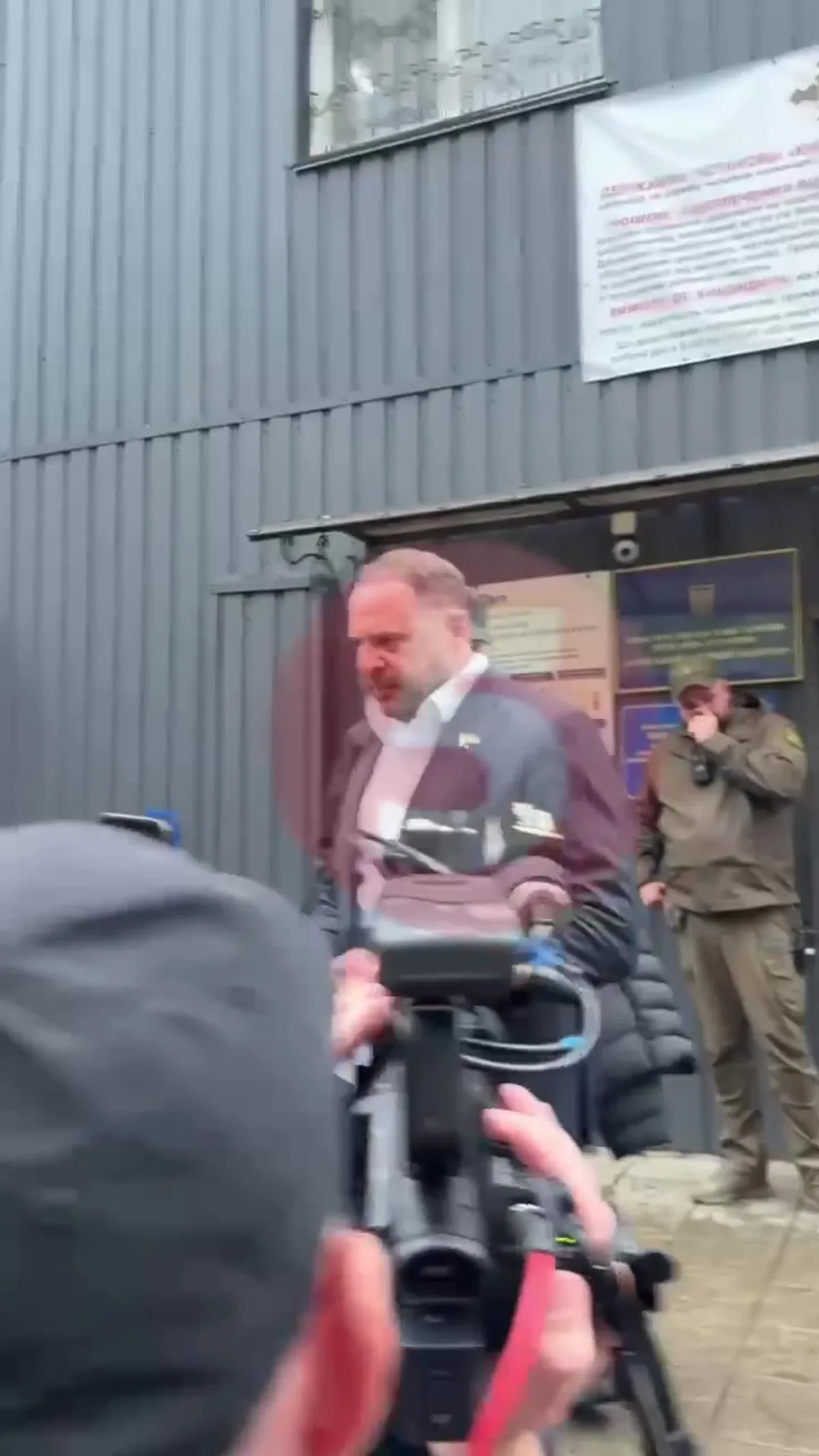 Чоловік у костюмі виходить з будівлі серед журналістів
