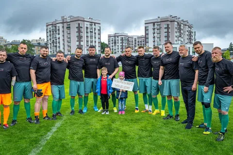 Футбольна команда в чорних футболках позує на полі біля багатоповерхових будинків