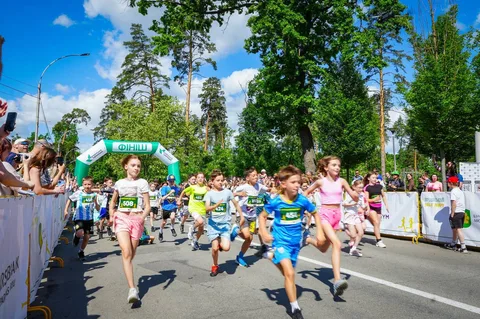 Дітьми та дорослі біжать на спортивному забігу під зеленою аркою