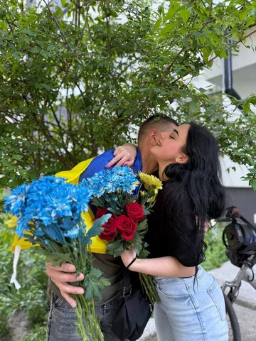Жінка тримає букет квітів і м'яку іграшку папуги