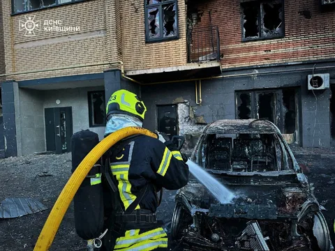 Рятувальник гасить пожежу в пошкодженому автомобілі біля будинку