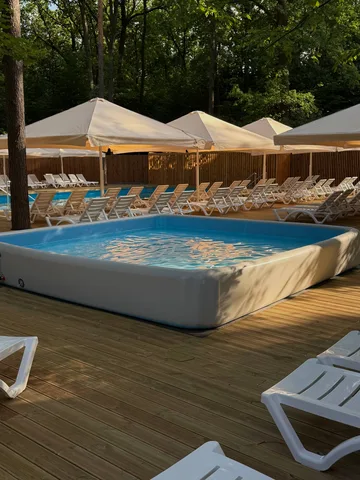 Басейн з блакитною водою на дерев'яному настилі під тентами