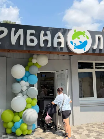 Людина з дитячим візком біля входу до магазину з кольоровими повітряними кулями