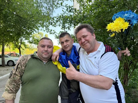Три чоловіки позують на фоні жовто-синіх квітів