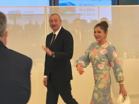 Чоловік у чорному костюмі та жінка у квітковій сукні на сцені форуму