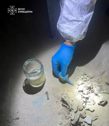 Рука в синій рукавиці збирає зразок речовини в скляну банку
