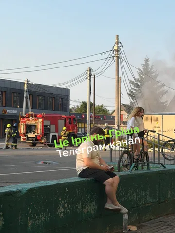 Людина сидить на бордюрі біля пожежної машини та диму