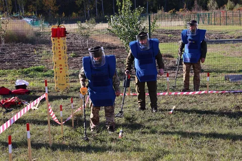 Сапери в синій формі розмінюють поле з червоно-білими маркерами