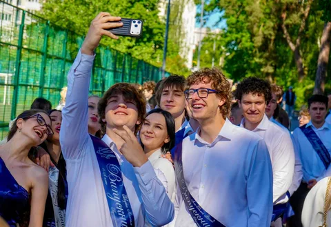 Група випускників у білих сорочках робить селфі на святкуванні